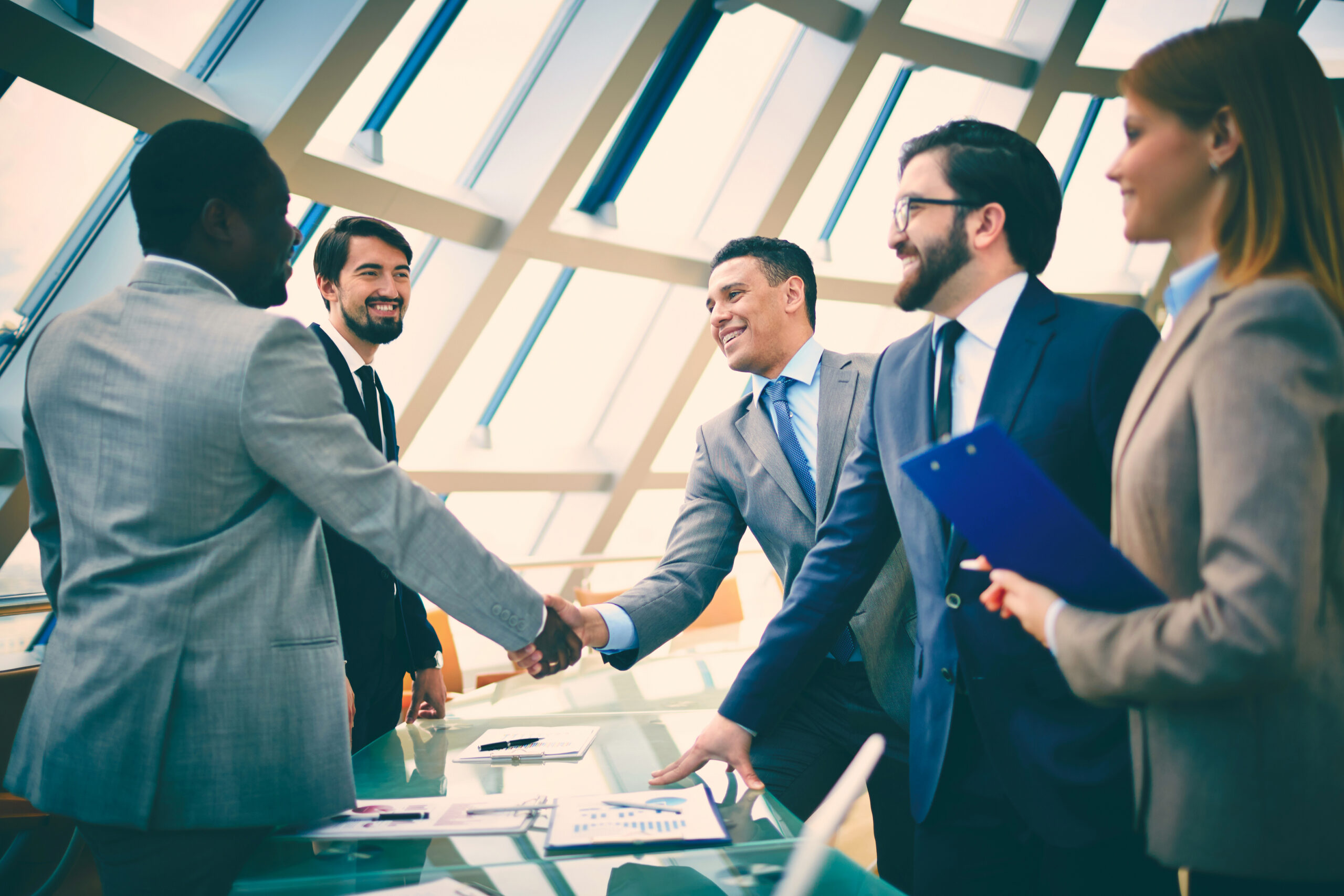 A group of sharply dressed business people in an office shaking hands as a sign of business partnership.